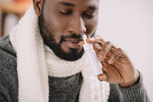 ill african american man in warm scarf with nose spray - Foto, afbeelding