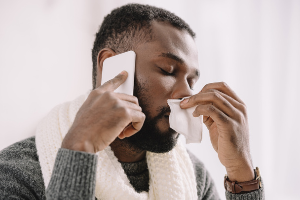 homme afro-américain malade avec nez qui coule tenant serviette tout en parlant sur smartphone
 - Photo, image