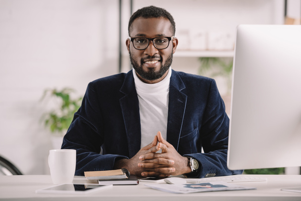 スタイリッシュなアフリカ系アメリカ人のビジネスマンがオフィスにあるコンピューターでの作業を笑顔 - 写真・画像