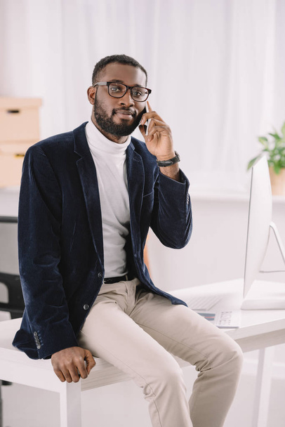 красивий афроамериканський бізнесмен говорить смартфон, сидячи на столі
  - Фото, зображення