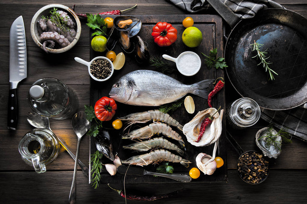 op view of fresh sea food on grunge textured black background. Shrimps, bream, herbs, lemon - Фото, зображення