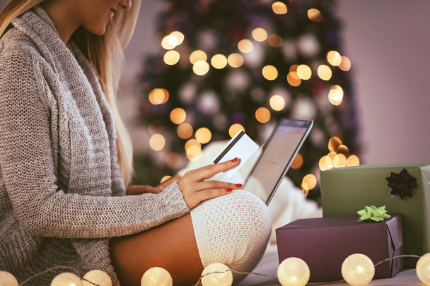 Happy young woman relaxing at home and online buying Christmas presents on laptop. - Fotografie, Obrázek