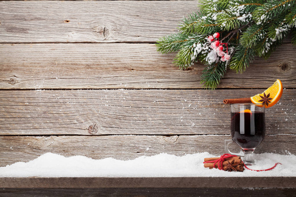 Cup of mulled wine with spices and fir tree branch covered by snow on wooden background - Photo, Image