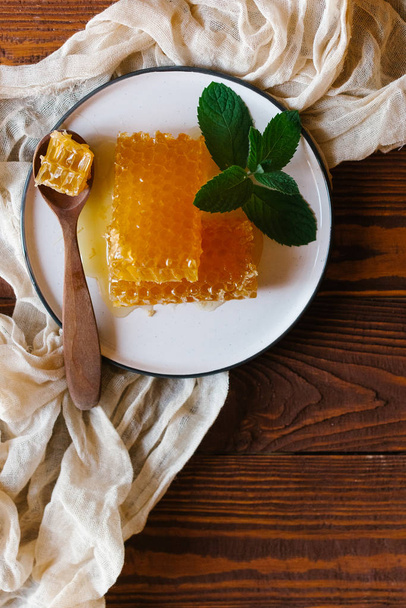 Вид сверху свежих медовых гребешков, украшенных мятой с деревянной ложкой на белой тарелке поверх бежевой льняной ткани
 - Фото, изображение