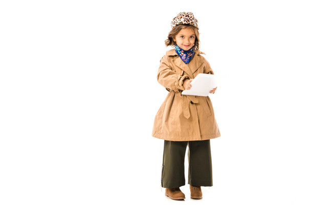 adorable little child in trench coat using tablet and looking at camera isolated on white - Foto, Imagem