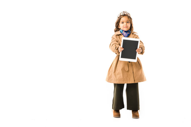 beautiful little child in trench coat showing tablet with blank screen isolated on white - Photo, Image
