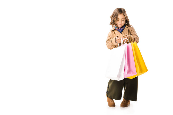 beau petit enfant en trench coat tenant des sacs à provisions colorés isolés sur blanc
 - Photo, image
