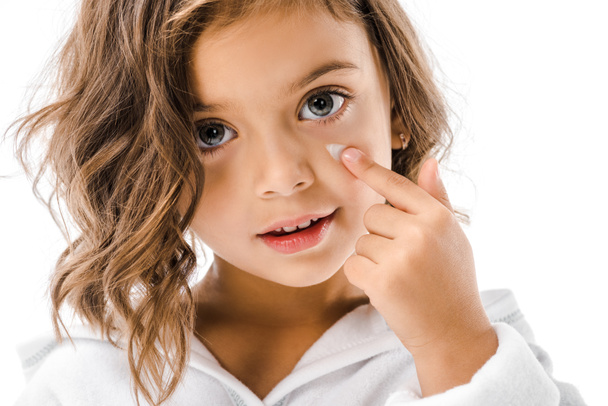 Porträt eines kleinen Kindes, das auf Gesichtscreme isoliert auf Weiß aufträgt - Foto, Bild