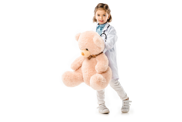 kid dressed in doctors white coat with stethoscope holding big teddy bear isolated on white - Foto, Imagem