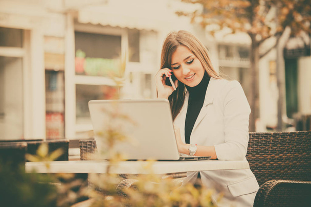 Szczęśliwy przedsiębiorca nowoczesne i atrakcyjne kobiety pracy z telefonu i laptopa w kawiarni przy ulicy - Zdjęcie, obraz