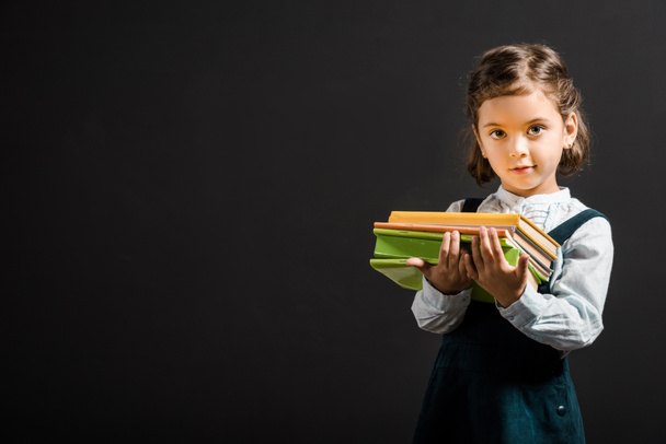 portrait of adorable schoolchild holding books isolated on black - Photo, Image