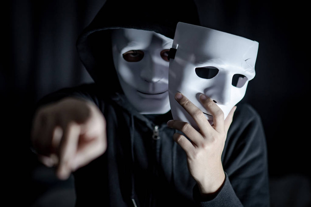 Geheimnisvoller Kapuzenmann, der seine Hand zeigt und eine zerbrochene weiße Maske hält. Anonyme soziale Maskierung. schwere depressive Störung oder bipolare Störung. Halloween-Konzept - Foto, Bild