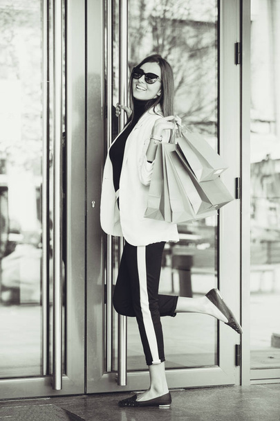 Happy young woman with shopping bags entering shop. Happy woman going into a store. Black and white photo - Фото, зображення