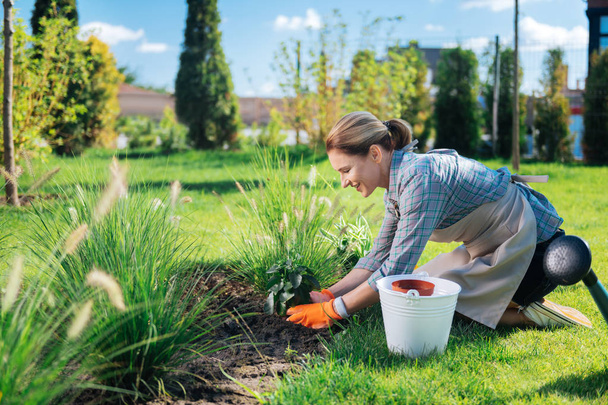 Happy appealing woman smiling while putting little green plant in the soil - Foto, Bild