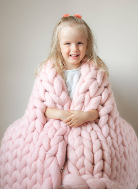 Beautiful Little Happy Blond Ginger Girl Sitting on Bed with a Pink Merino Woolen Knitted Giant Plaid Blanket - Foto, Imagem