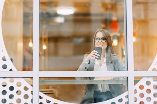 Blogger menina com café sentado em uma cafeteria e trabalhando. Laptop e telefone na mão. Estilo de negócios em roupas
. - Foto, Imagem