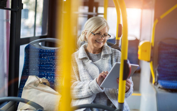 Senior kobiety za pomocą tabletu, podczas jazdy autobusem - Zdjęcie, obraz