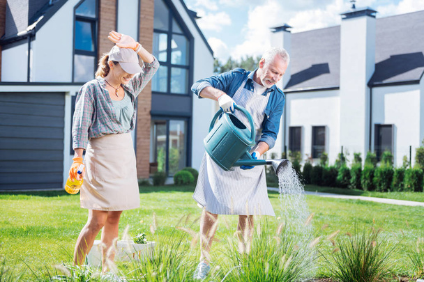 Husband and wife wearing casual clothes and aprons watering their garden bed - Photo, Image