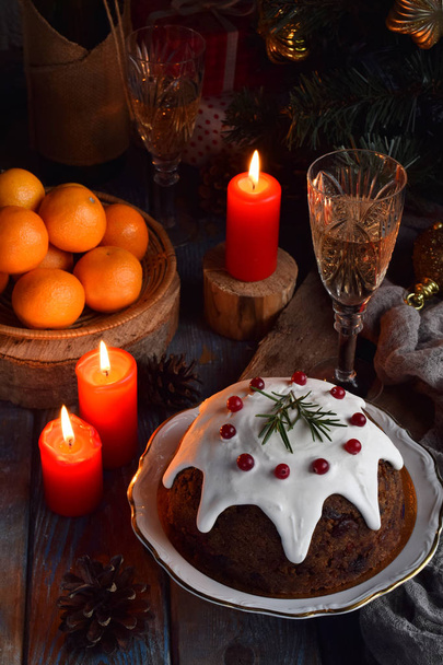 Παραδοσιακά ελληνικά Χριστούγεννα στον ατμό Πουτίγκα με χειμερινά μούρα, αποξηραμένα φρούτα, καρύδι στο εορταστικό σκηνικό με Χριστουγεννιάτικο δέντρο και καίγοντας κερί. Κέικ φρούτων - Φωτογραφία, εικόνα
