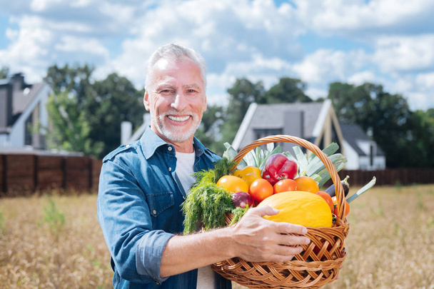 Dark-eyed farmer holding basket full of red sweet peppers and tomatoes - Φωτογραφία, εικόνα