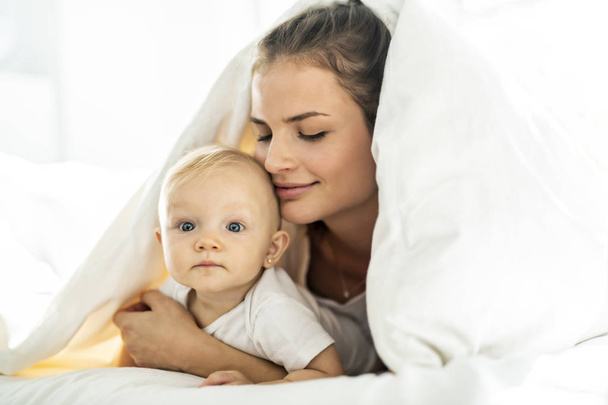 Portrait de jeune mère avec bébé fille couché sur le lit recouvert d'une couverture blanche
 - Photo, image