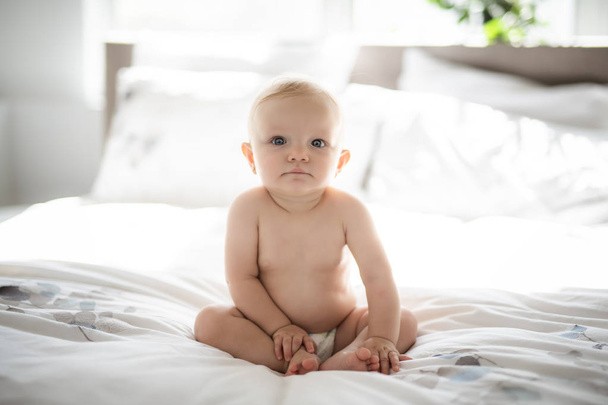 Cute baby girl sit on white sheet at home - Foto, afbeelding
