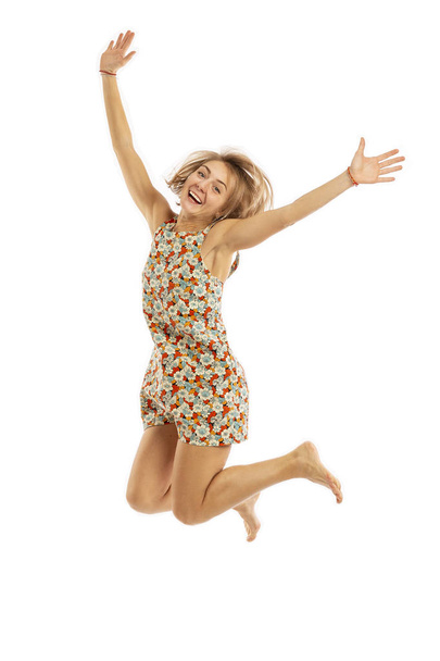 Jong meisje in een lichte jurk en blote voeten in een sprong, geïsoleerd op witte achtergrond - Foto, afbeelding