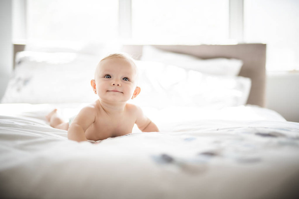 Cute baby girl lying on white sheet at home - Foto, afbeelding