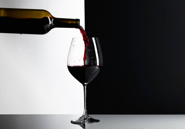 Rode wijn wordt gegoten in een glas. Reflexieve achtergrond, kopie ruimte voor uw tekst. - Foto, afbeelding