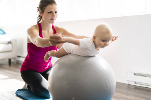 A Portrait of beautiful young mother in sports wear with her charming little baby in training session - Foto, imagen