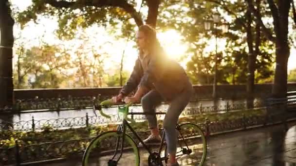 Pretty caucasian female riding a bicycle in the morning park or boulevard. Side view of a young woman riding a trekking bike, wearing sneakers and casual clothes - Materiaali, video