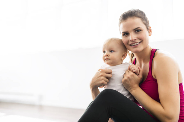A Portrait of beautiful young mother in sports wear with her charming little baby in training session - Φωτογραφία, εικόνα