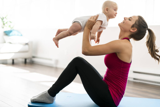 Portrait of beautiful young mother in sports wear with her charming little baby in training session - Foto, imagen