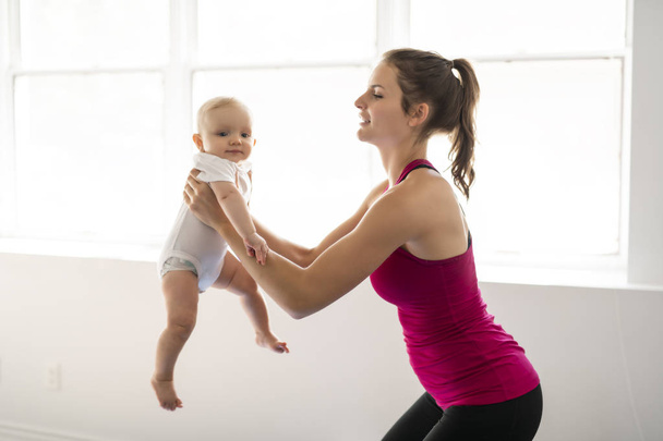 A Portrait of beautiful young mother in sports wear with her charming little baby in training session - Foto, immagini