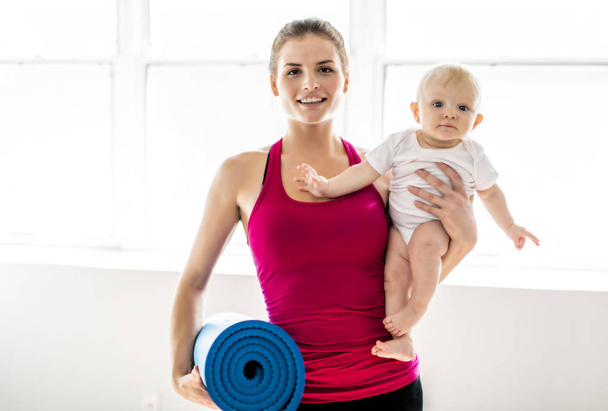 A Portrait of beautiful young mother in sports wear with her charming little baby in training session - Фото, зображення