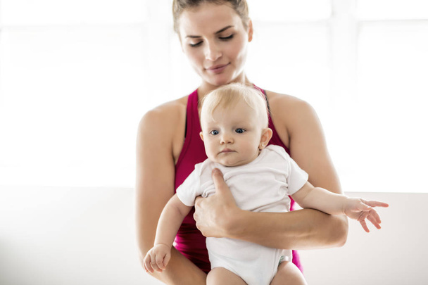 ein Porträt der schönen jungen Mutter in Sportkleidung mit ihrem charmanten kleinen Baby im Training - Foto, Bild