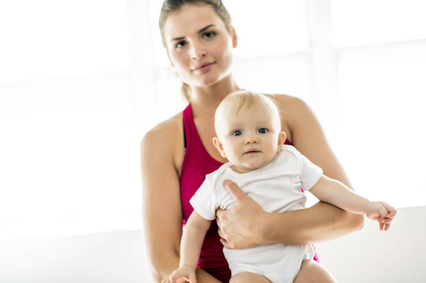 A Portrait of beautiful young mother in sports wear with her charming little baby in training session - Foto, Bild