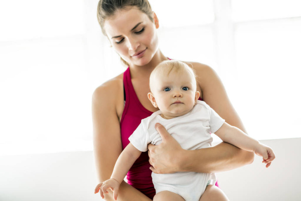A Portrait of beautiful young mother in sports wear with her charming little baby in training session - Foto, Imagen