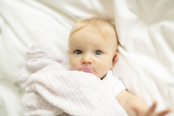 A cute baby with pacifier lying on a white bed - Foto, Imagen