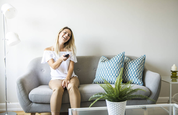Women watching TV on the sofa at home with remote control - Foto, imagen