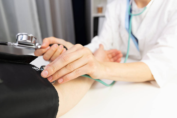 A female doctor measuring blood pressure of a man in a doctors office. - Foto, Bild