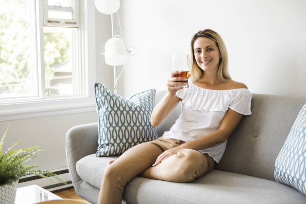 Woman drinking beer sitting on a couch in the living room at home - Φωτογραφία, εικόνα