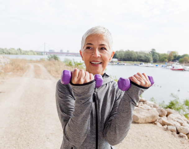 Femme mûre en bonne santé faisant de l'exercice avec des poids, cheveux gris-courts, vêtements de sport, entraînement en plein air
 . - Photo, image