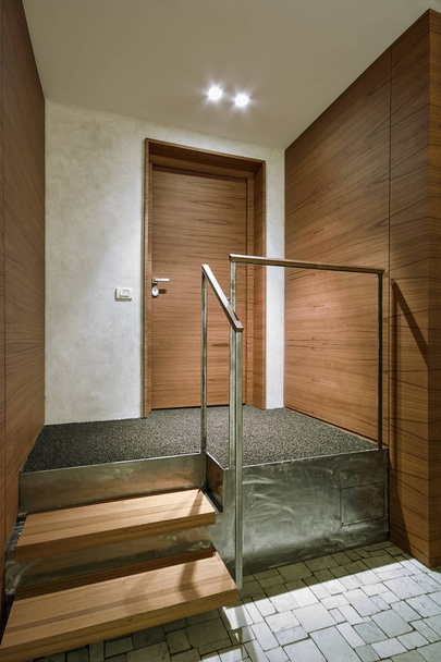 internal shots of the entrance of a apartment with wainscoting in the foreground some wooden steps and the steel handrail in the bottom the wooden main door  - Fotoğraf, Görsel