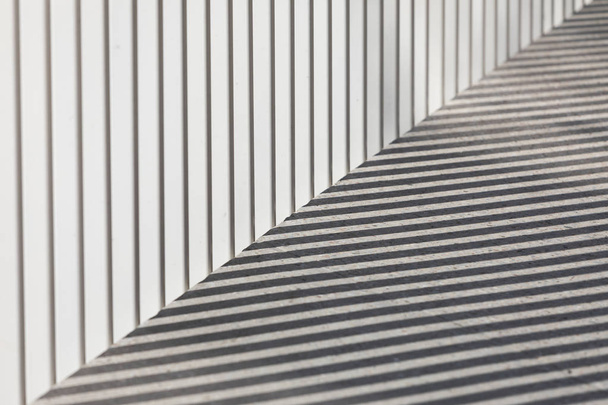 Σκιές που χαϊδεύονται από φράχτη σε τσιμεντένιο πεζοδρόμιο - Φωτογραφία, εικόνα