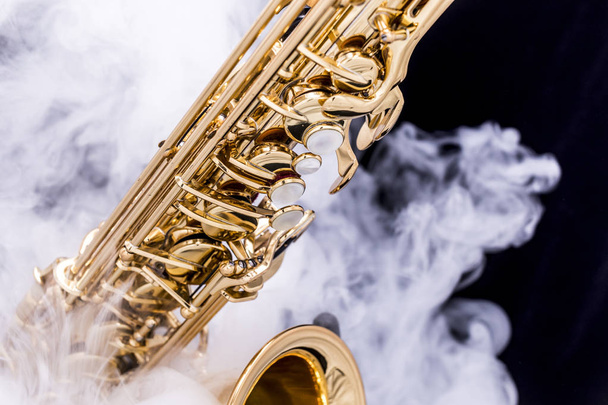 A gold plated saxophone in smoke on a black background - Foto, imagen