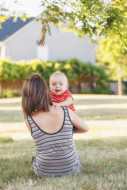 Group portrait of Caucasian mother with baby boy in red t-shirt in field meadow outside. Female parent holding little happy smiling son child in summer park on sunset. Happy parenting lifestyle. - Zdjęcie, obraz
