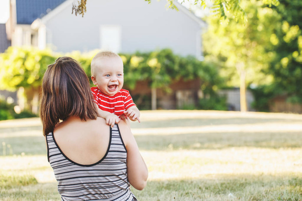 Ομάδα πορτρέτο του Καυκάσου μητέρα με μωρό αγόρι στο κόκκινο t-shirt σε πεδίο Λεϊμόνες εκτός. Θηλυκό μητρική εκμετάλλευση λίγο ευτυχισμένη χαμογελαστό παιδί γιος στο πάρκο καλοκαίρι στο ηλιοβασίλεμα. Ευτυχείς γονείς lifestyle. - Φωτογραφία, εικόνα