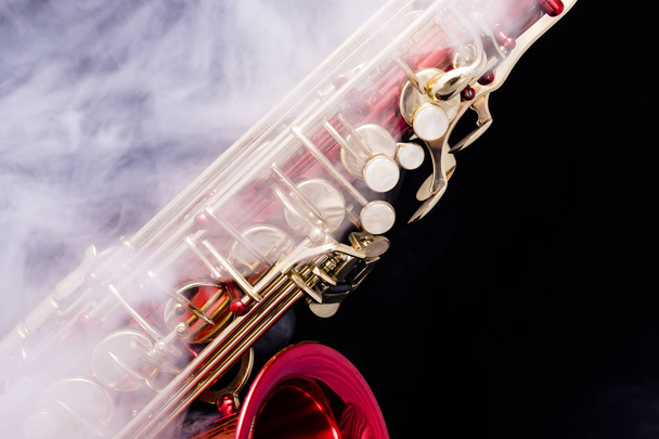 Um saxofone lacado vermelho com chaves banhadas a ouro em fumaça em um fundo preto
 - Foto, Imagem
