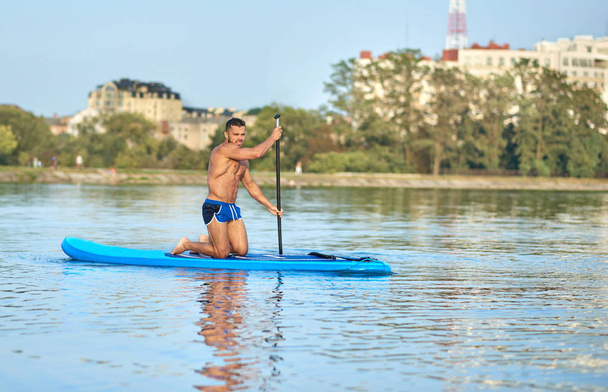 Boy on paddle board rowing in middle of city lake. - Fotó, kép